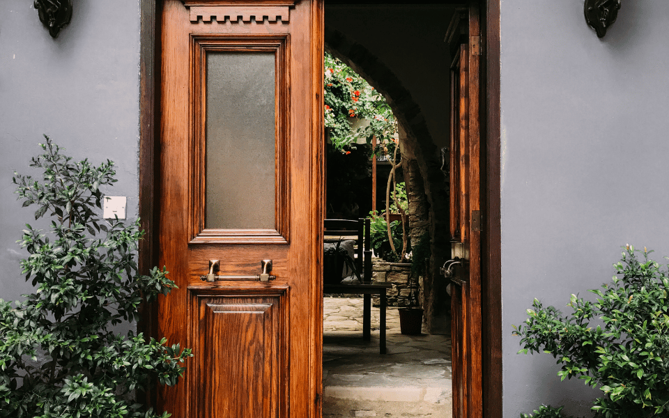 Puerta de madera barnizada instalada profesionalmente, abierta para mostrar un jardín interior, resaltando la calidad del trabajo y la belleza del acabado.