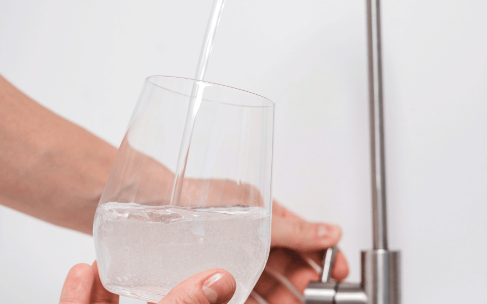 Mano llenando un vaso de agua filtrada desde un grifo de cocina.